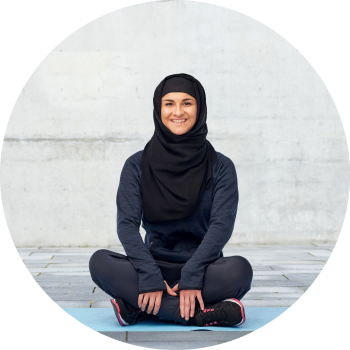 Woman in all black sports hijab sitting with crossed legs and smiling